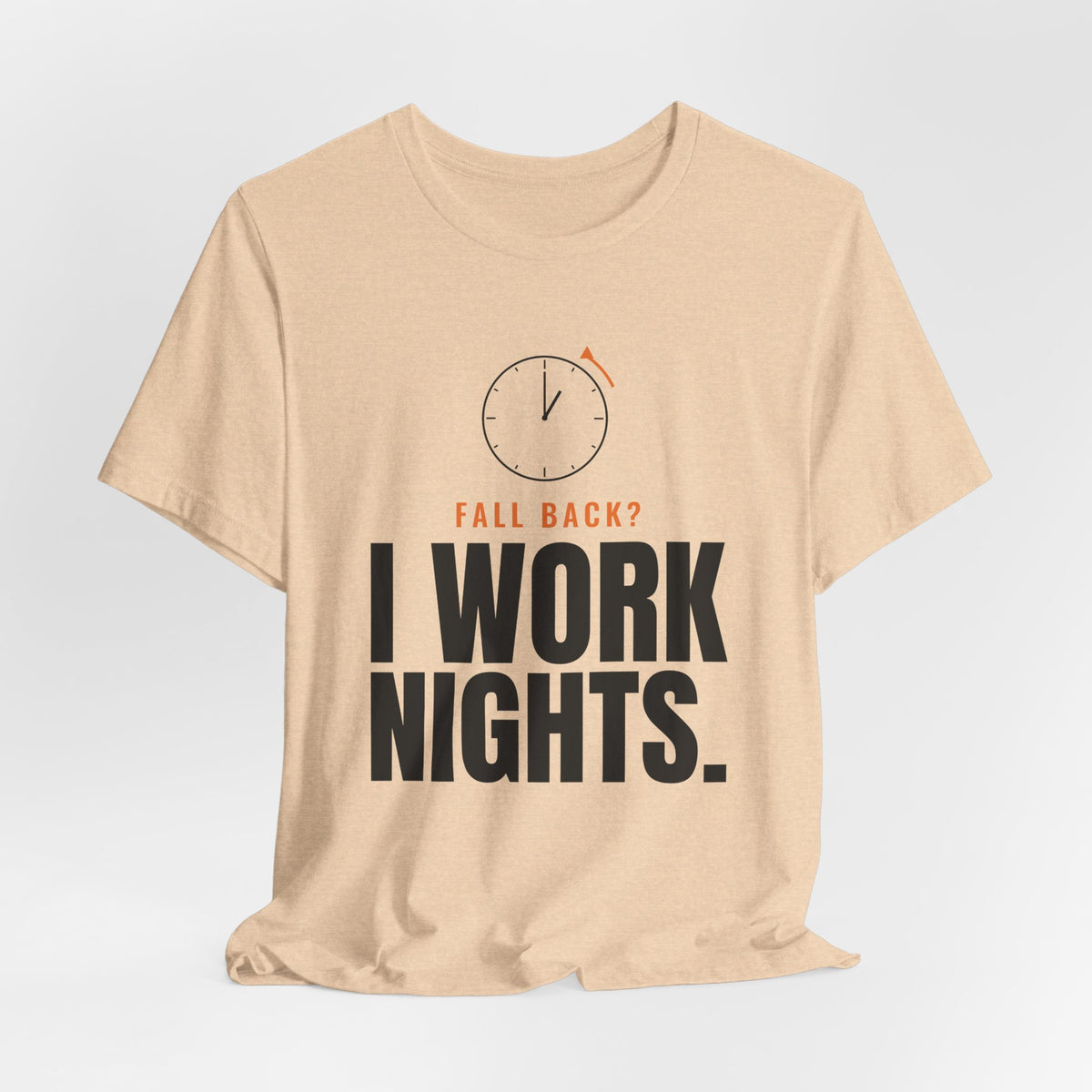 Natural tan night shift tee with a clock turning back and "FALL BACK? I WORK NIGHTS." in orange and bold type, on a soft gray backdrop