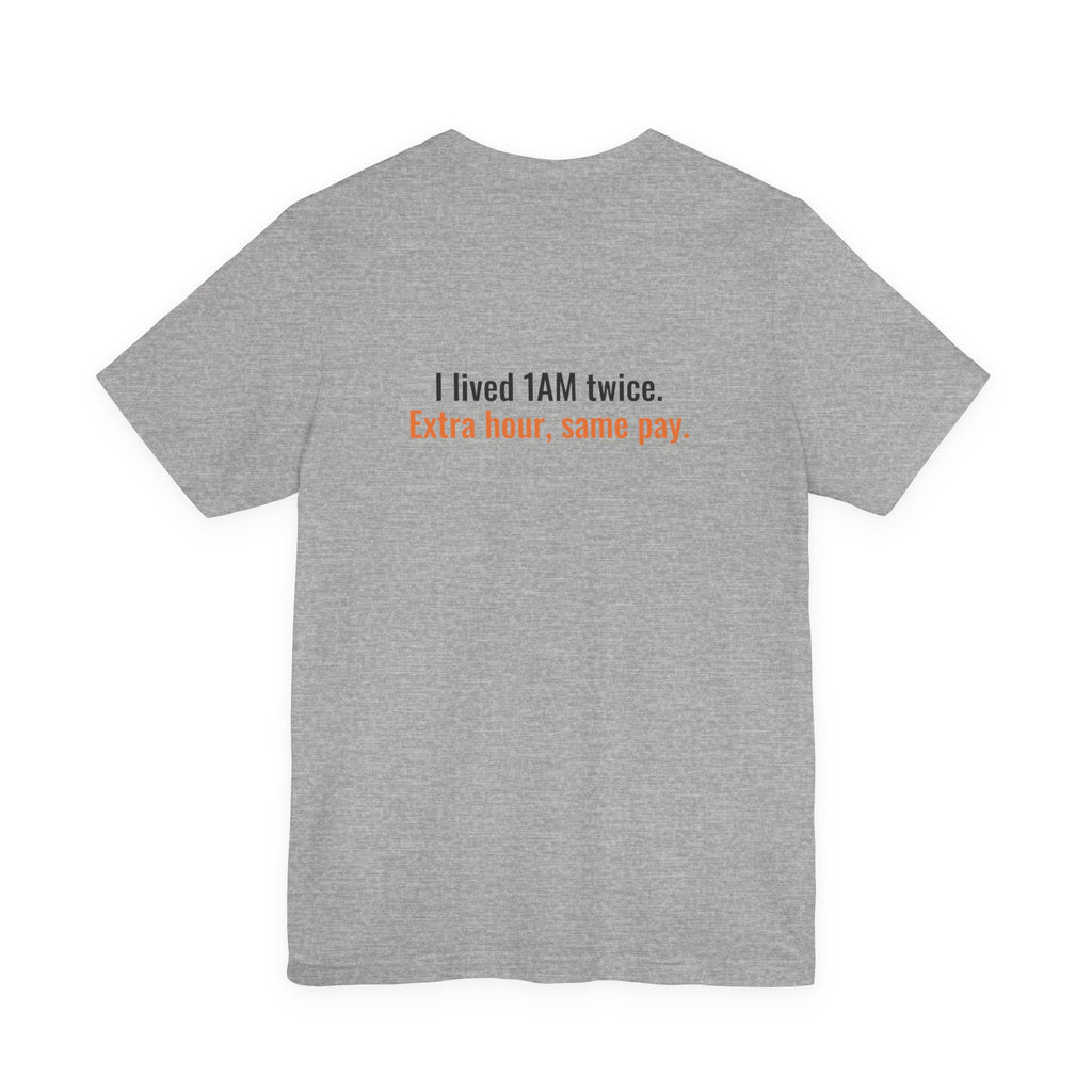 Back of the heather gray tee printed with the small slogan "I lived 1AM twice. Extra hour, same pay."