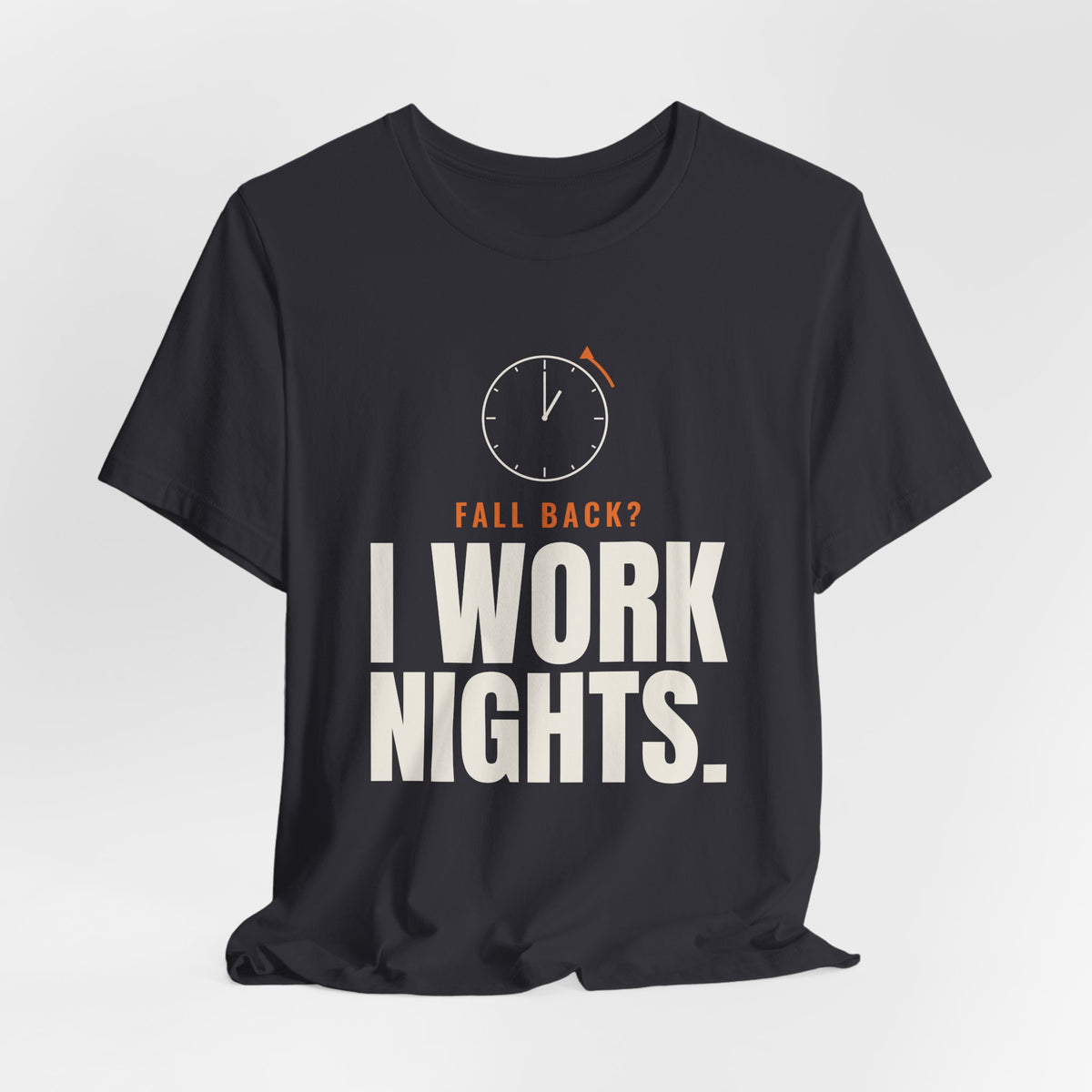 Charcoal night shift tee with a clock turning back and "FALL BACK? I WORK NIGHTS." in orange and bold type, on a soft gray backdrop